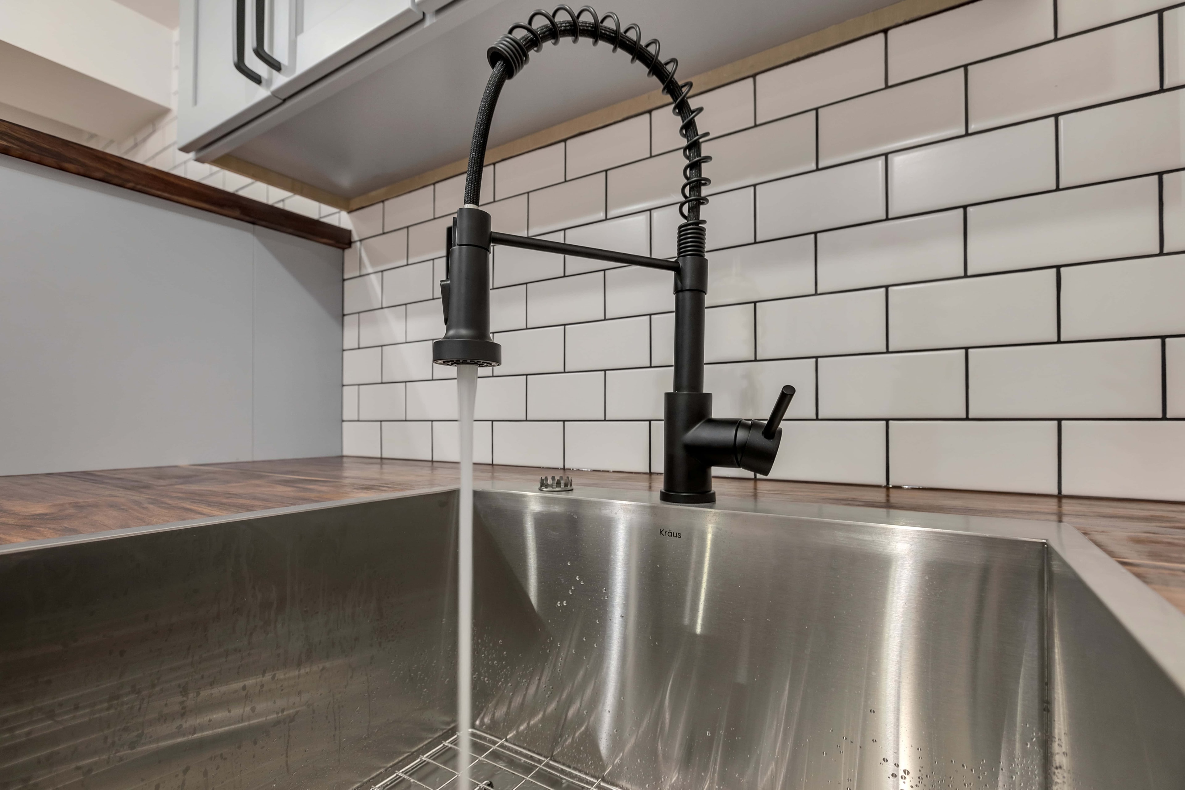 Matte black coil spring faucet detail — stainless undermount sink, white subway tile backsplash, eco-friendly kitchen remodel Maryland