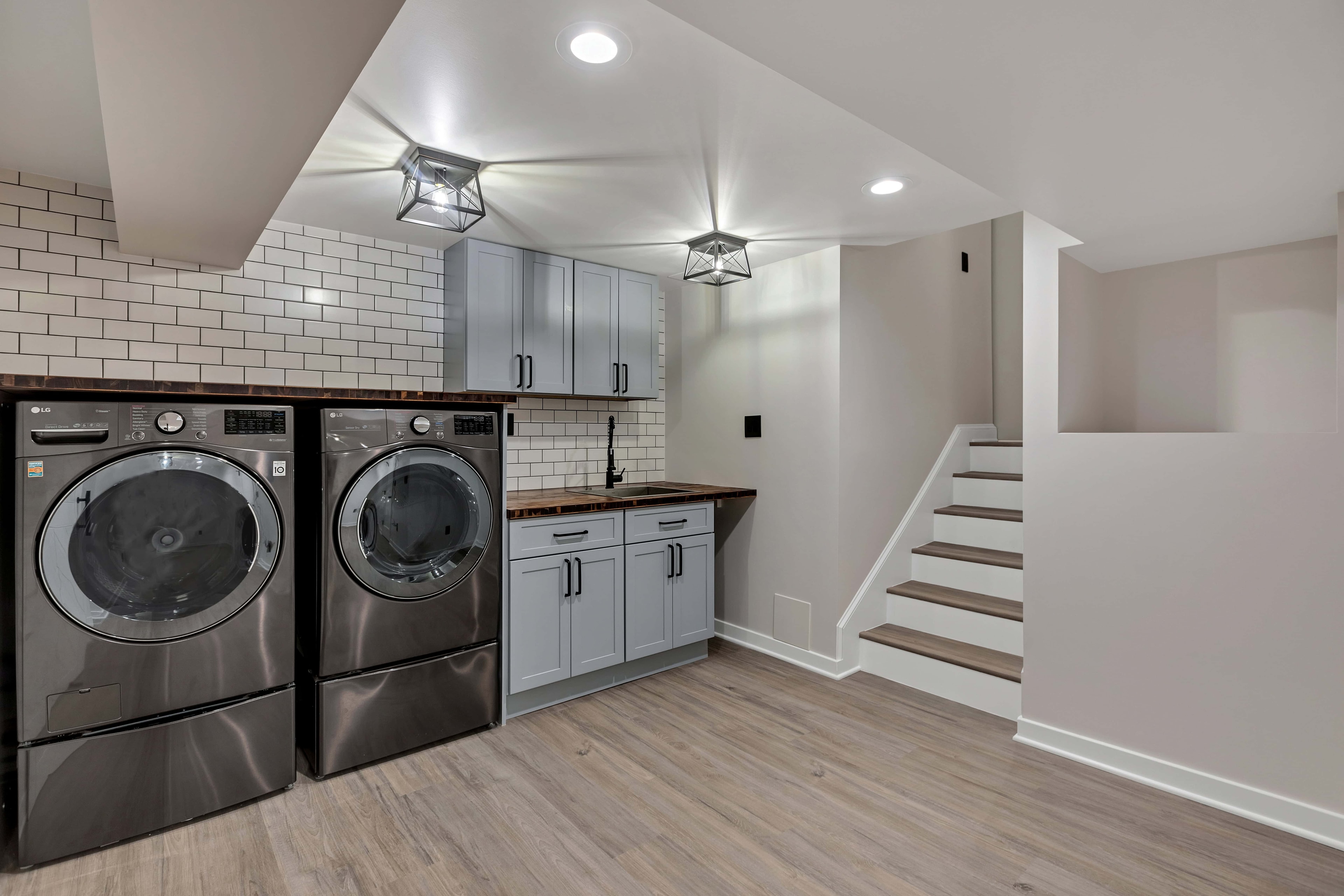 Gray shaker base cabinets with walnut butcher block countertop — matte black pulls and coil faucet, sustainable laundry room remodel Maryland