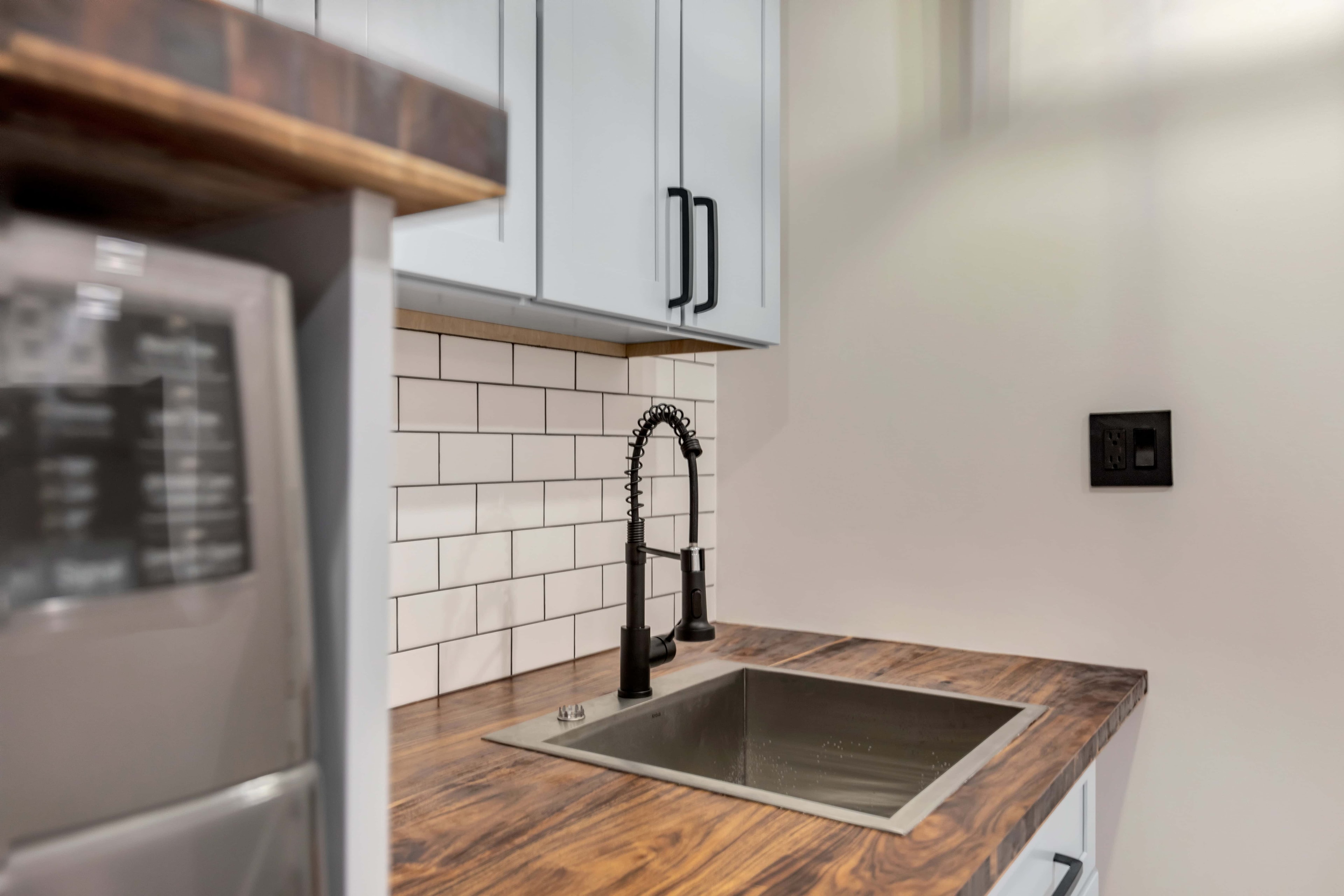 Wide laundry sink area Maryland — gray upper and lower shaker cabinets, walnut countertop, subway tile, matte black faucet, eco-friendly renovation