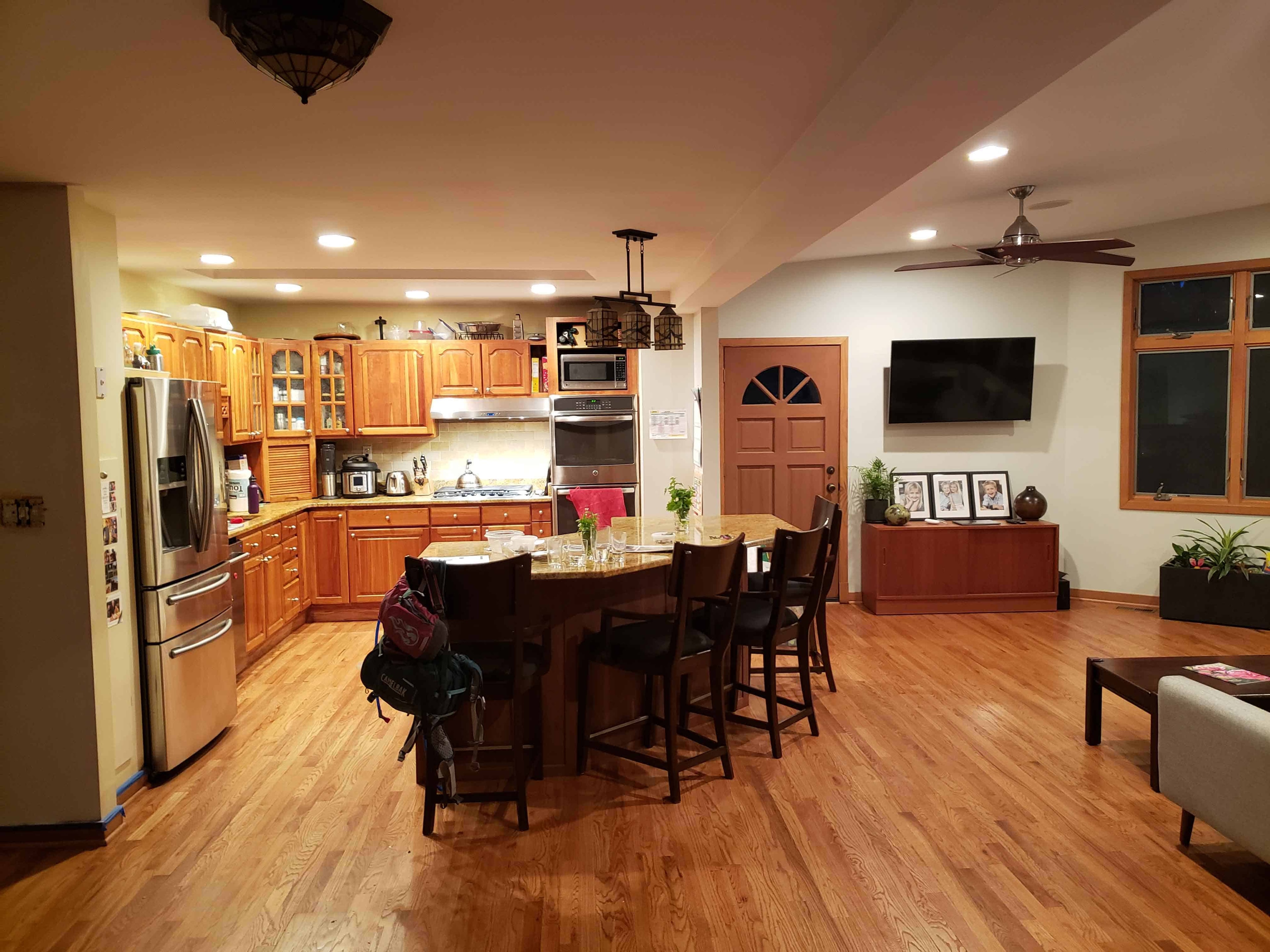 Open concept kitchen and living room before renovation Maryland — warm wood cabinets, island seating, hardwood floors